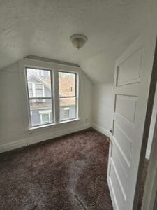 Attic bedroom with sloped ceiling freshly painted white, including window trim, baseboards and five-panel door