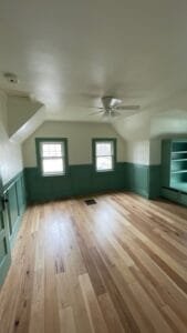 Attic room with green painted wainscoting, window trim and built-in bookshelves beneath cream walls and sloped ceiling