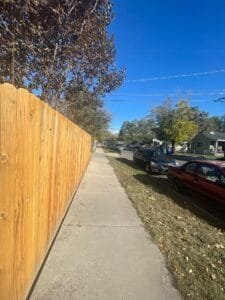 Freshly stained golden wood fence running along a neighborhood sidewalk