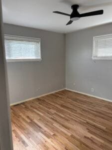 Bedroom with light gray walls showing patched spots before painting, black ceiling fan and oak floors