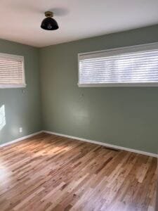 Bedroom freshly painted soft sage green with white ceiling and trim, black dome light and oak floors