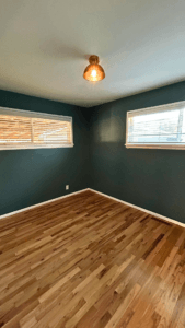 Bedroom corner painted deep teal with white baseboards, brass ceiling light and oak floors
