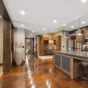 Finished basement with glossy stained concrete floor, rustic wood beams and a kitchenette island