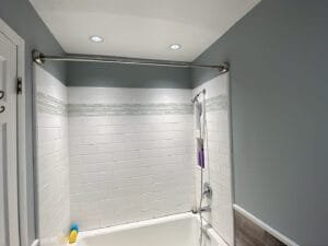 Bathroom walls painted slate blue-gray around a white subway tile tub surround with a glass mosaic accent band