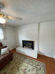 Brick fireplace and raised hearth painted white in a living room with off-white walls and hardwood floors