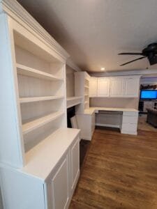 Built-in bookshelves and corner desk cabinetry painted crisp white with crown molding in a home office