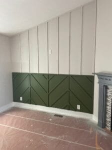Accent wall with olive green chevron wainscoting below white board and batten paneling under a sloped ceiling