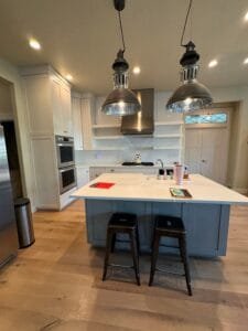 Kitchen with painted white shaker cabinets and a blue-gray island under industrial pendant lights