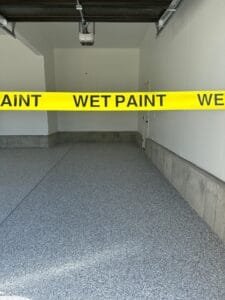 Newly coated gray flake garage floor behind yellow Wet Paint caution tape