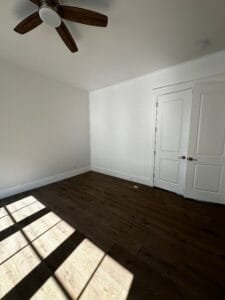 Empty bedroom with freshly painted white walls, crisp white baseboards and paneled closet doors in afternoon sunlight