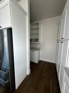 Walk-in pantry painted white with white shaker cabinets, open shelving and dark hardwood floors