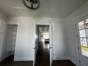 Home office freshly painted bright white with white double doors, built-in shelving and dark hardwood floors