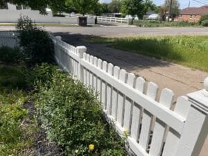 Freshly painted white wooden picket fence along a sidewalk with a garden bed of roses