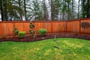 Backyard cedar fence stained warm red brown behind a mulched garden bed and lawn
