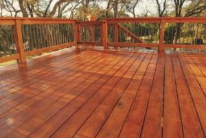 Glossy freshly sealed cedar deck with metal baluster railing and a gate to the stairs