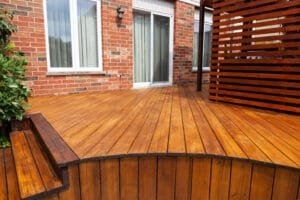 Curved wood deck with rich amber stain and slatted privacy screen behind a red brick house