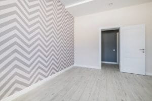 Empty room with a gray chevron wallpaper feature wall, white painted walls, trim and door