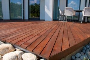 Freshly stained hardwood deck with patio furniture beside a modern home with glass doors