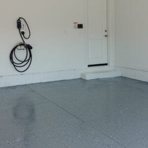 Garage corner with a gray flake epoxy floor coating, white painted walls and an EV charger
