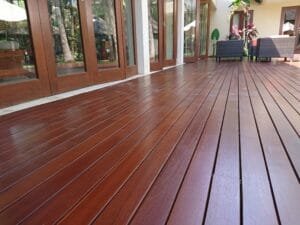 Close-up of glossy mahogany-stained hardwood deck boards beside wood-framed glass folding doors
