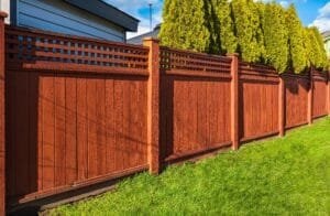 Wood privacy fence freshly stained reddish brown with lattice top panels beside a green lawn