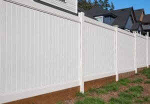 White privacy fence panels along a backyard with houses and blue sky behind