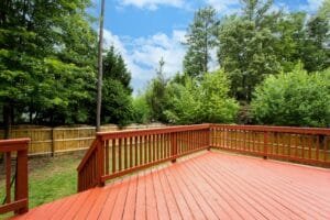 Backyard deck and railing coated in solid redwood stain overlooking a fenced lawn and trees