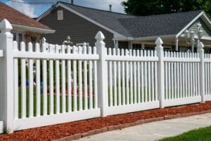 White picket fence with scalloped tops along a front yard with a gray sided house behind
