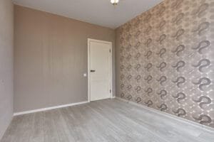Empty room with a retro patterned wallpaper accent wall beside taupe painted walls and a white door