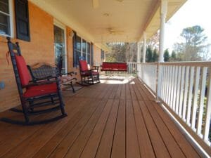 Covered front porch with brown stained floorboards, white railing and red-cushioned rocking chairs
