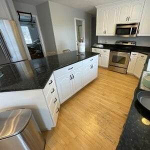 Kitchen with arched cabinet doors painted white, black granite countertops and an angled island