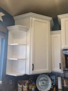 Upper kitchen cabinets and open corner shelves freshly painted white against a blue wall