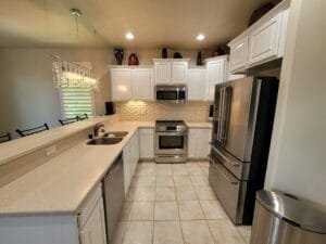 U-shaped kitchen with raised-panel cabinets painted bright white, cream countertops and a crystal chandelier