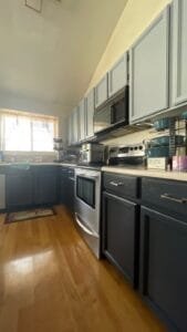 Kitchen with light blue-gray painted upper cabinets and charcoal lower cabinets under a vaulted ceiling