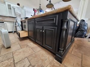 Kitchen island cabinets painted glossy black with turned legs while a painter refinishes white upper cabinets