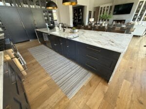 Large kitchen island and floor-to-ceiling cabinets painted dark navy with brass pulls and a marble waterfall top