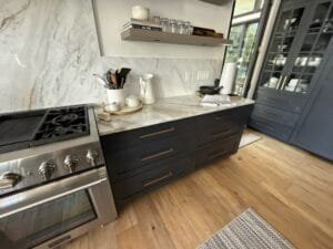 Navy painted drawer base cabinets with brass pulls beside a pro range and marble slab backsplash