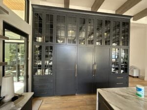 Floor-to-ceiling wall of navy painted cabinetry with mullioned glass doors and a panel-front refrigerator