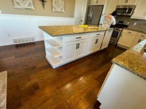 Kitchen island painted white with curved open end shelves, black pulls and gold granite as a painter works behind