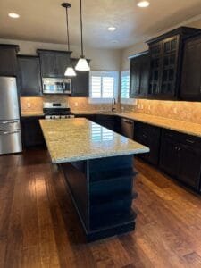 Before cabinet painting: kitchen with dark espresso stained cabinets, gold granite and a travertine backsplash