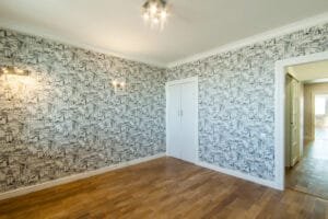 Empty room papered in black and white toile wallpaper with white painted trim and closet doors