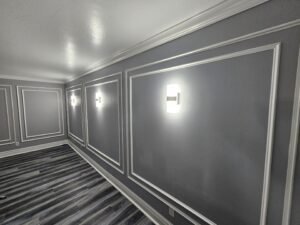 Room painted medium gray with white picture frame wall molding, crown molding and modern wall sconces