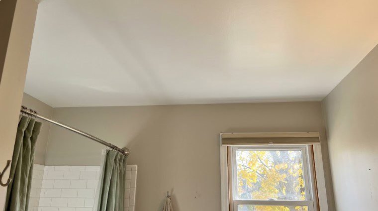 Smooth, repainted bathroom ceiling above a shower curtain and window